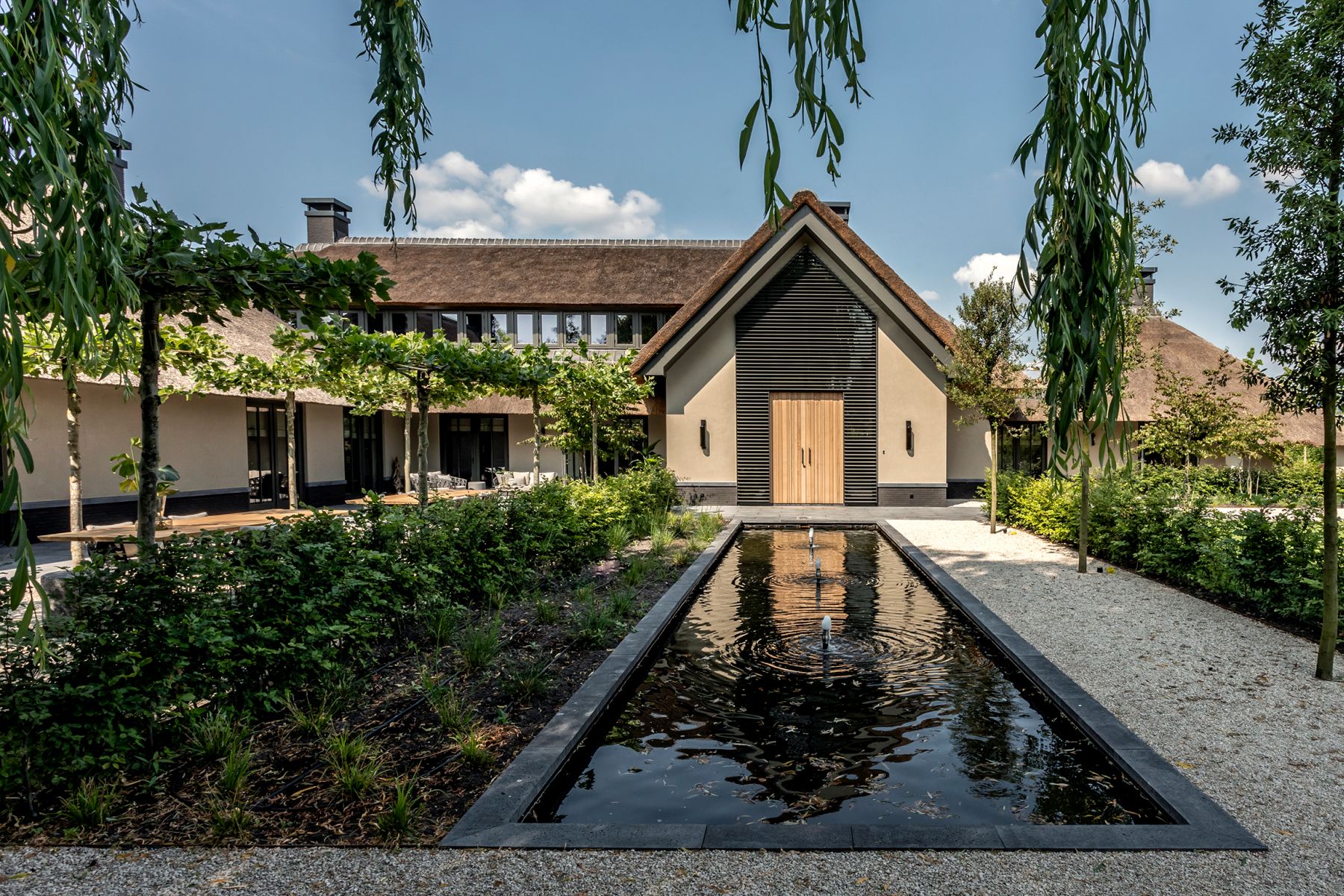 Rietgedekte villa met langwerpige waterpartij en grindpad