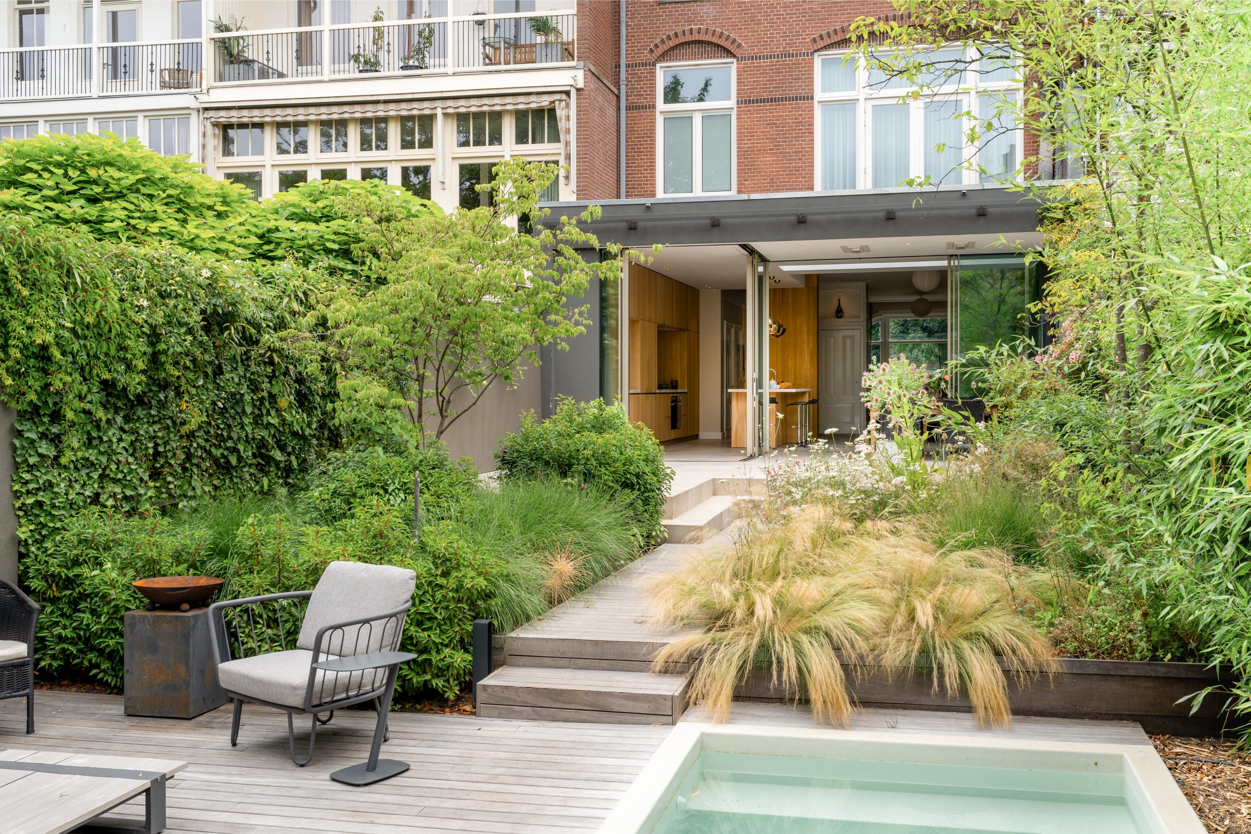 Tuinzijde woning met grijze uitbouw, houten deuren en groene beplanting