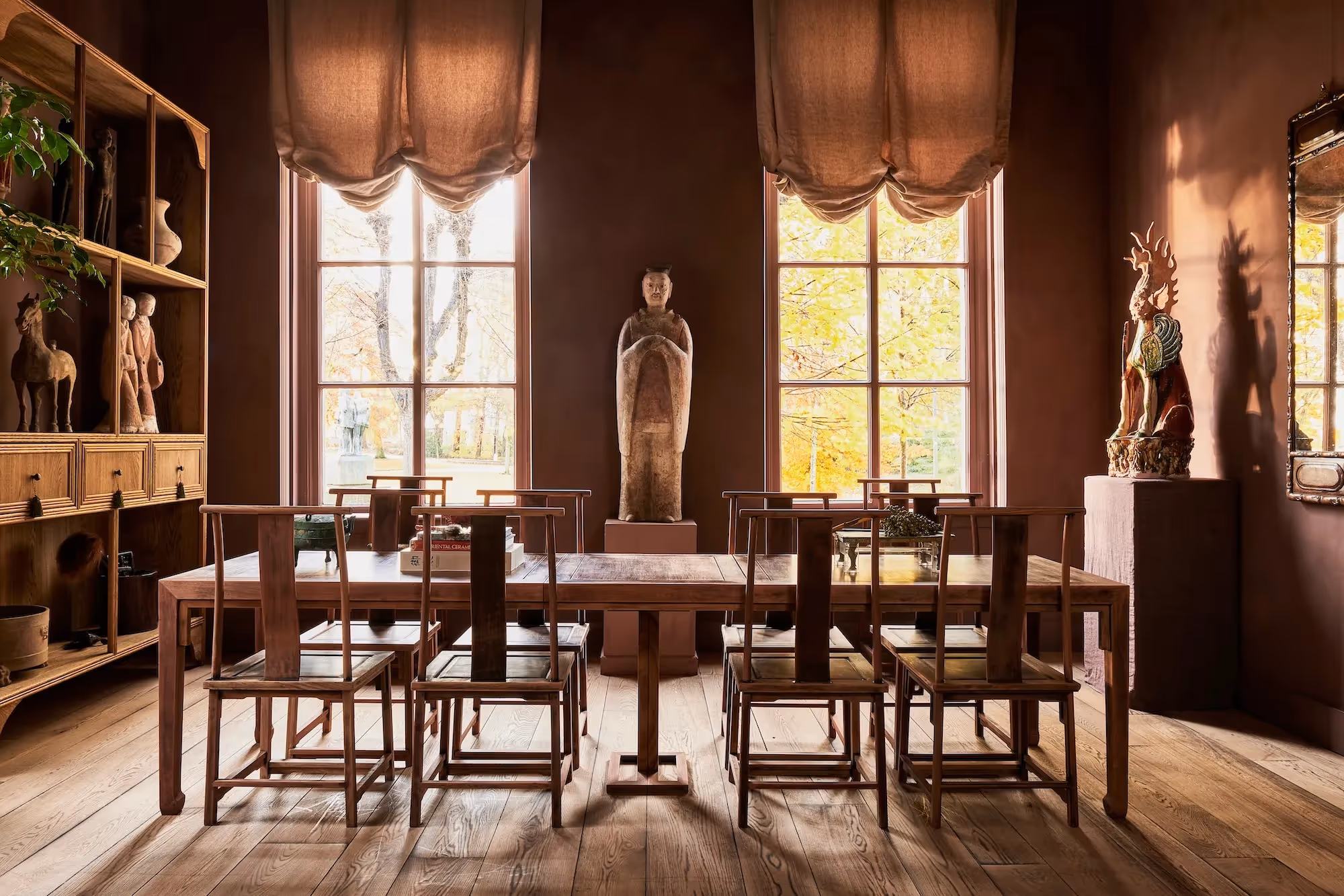 Eetkamer met houten tafel, stoelen en Chinese sculpturen tegen terracottamuren