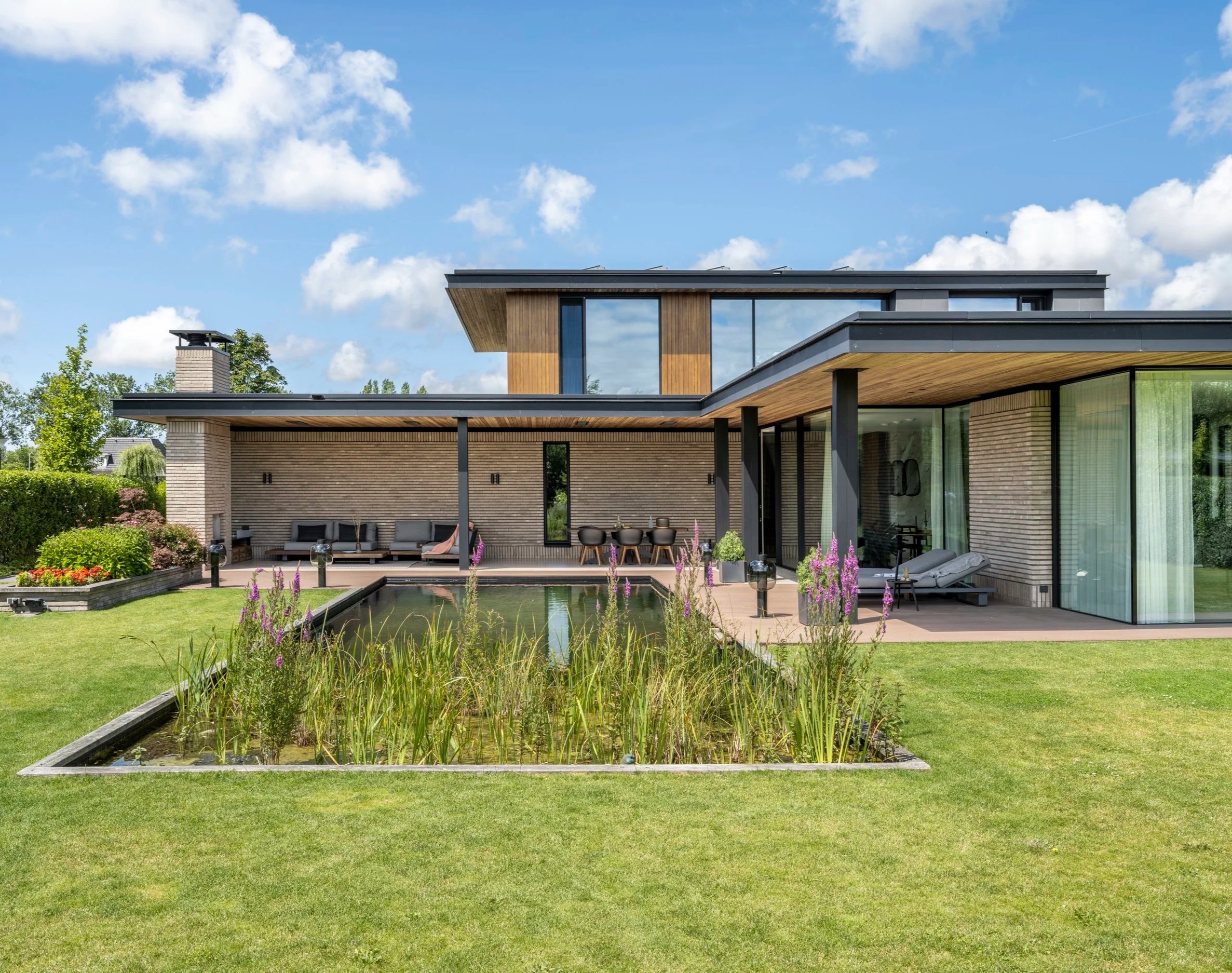 Hedendaagse woning met houtafwerking, terras en vijver in landschapstuin