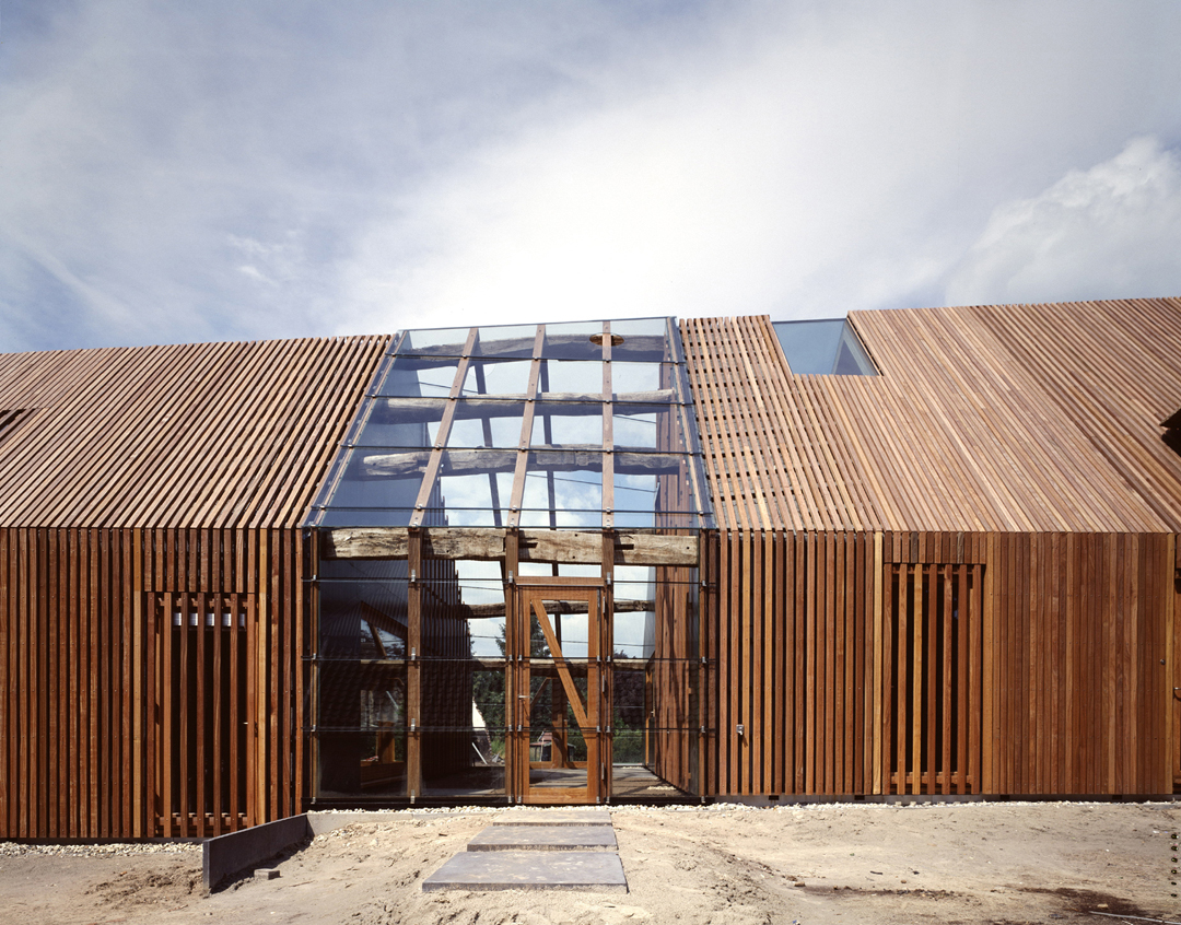 Moderne villa met houten gevelbekleding en glazen vooringang op zandpad