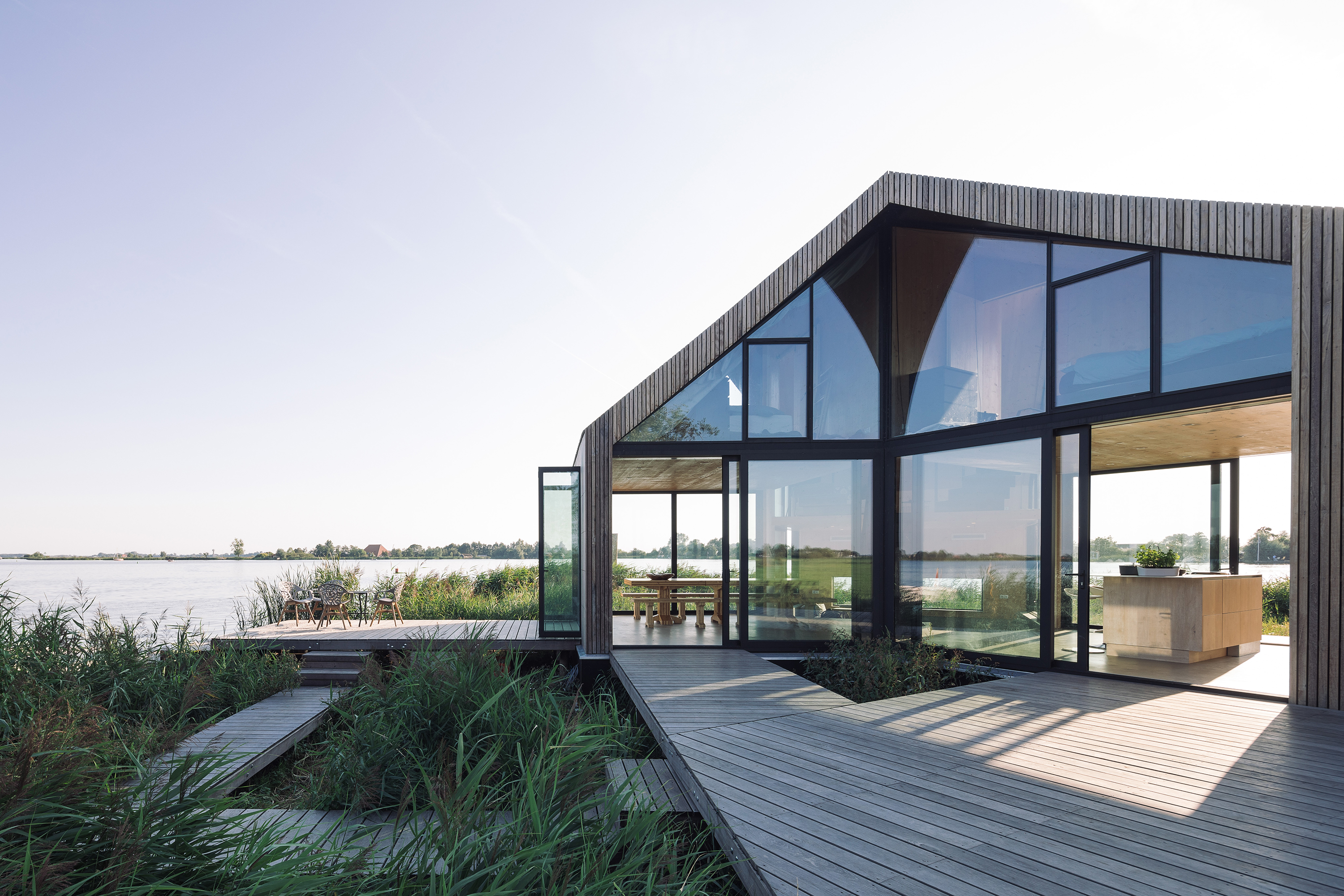 Moderne villa met golfplaten gevel, glazen voorgevel en houten terras aan waterkant