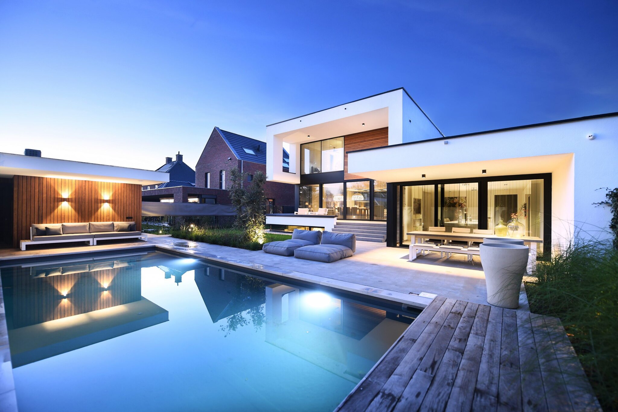 Luxe villa met houten lounge, zwembad en verlichte houten dek 's avonds