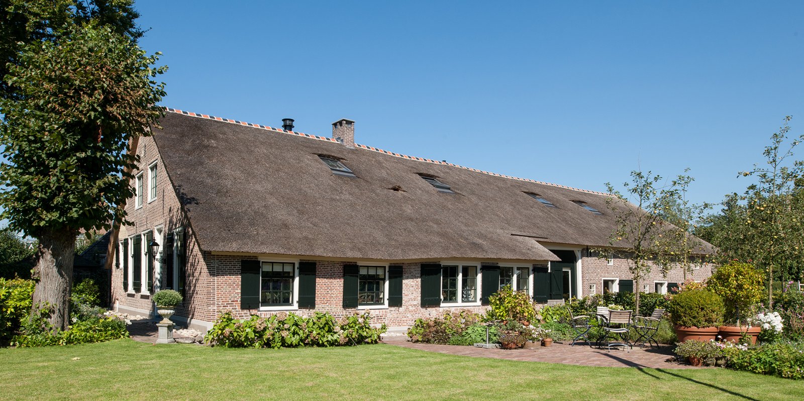 Voorgevel rietgedekt landhuis met bakstenen muren en groene omgeving