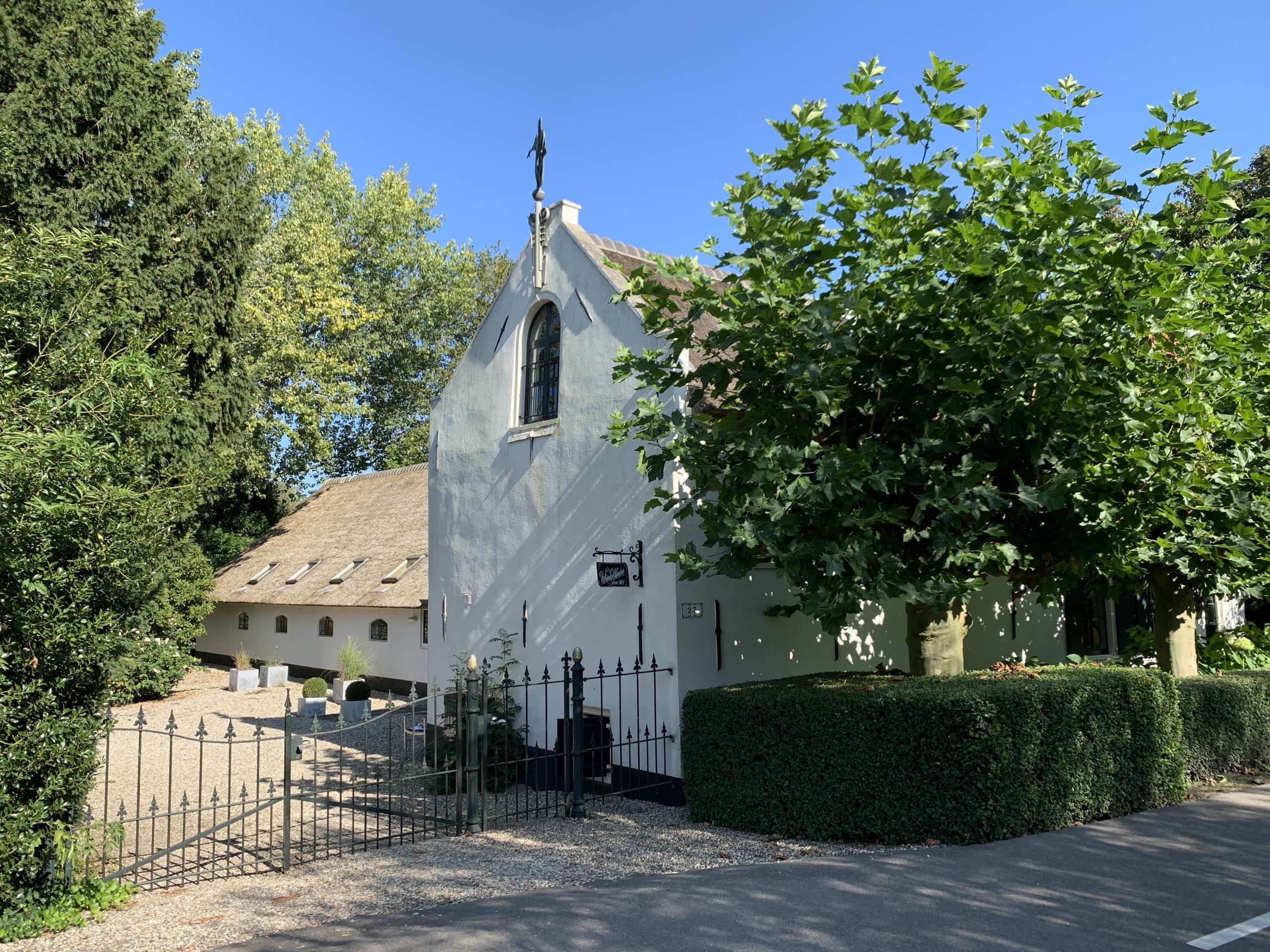 Witte kapel met spitse toren omgeven door groen en hagen